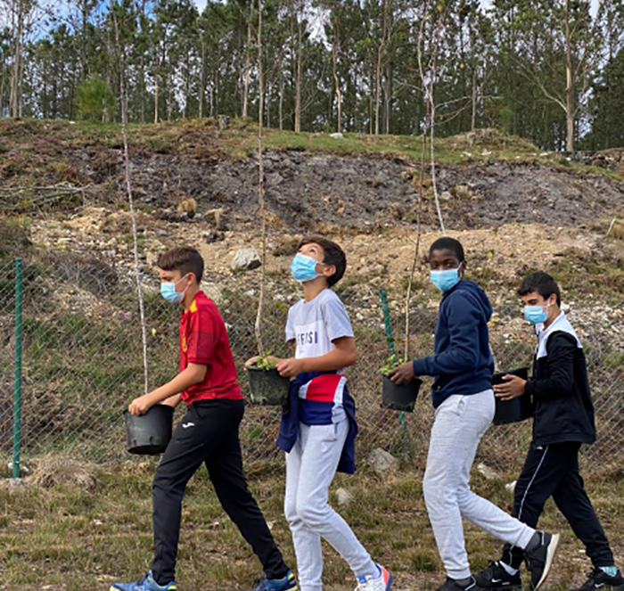 Cuatro estudiantes con plantones de árboles